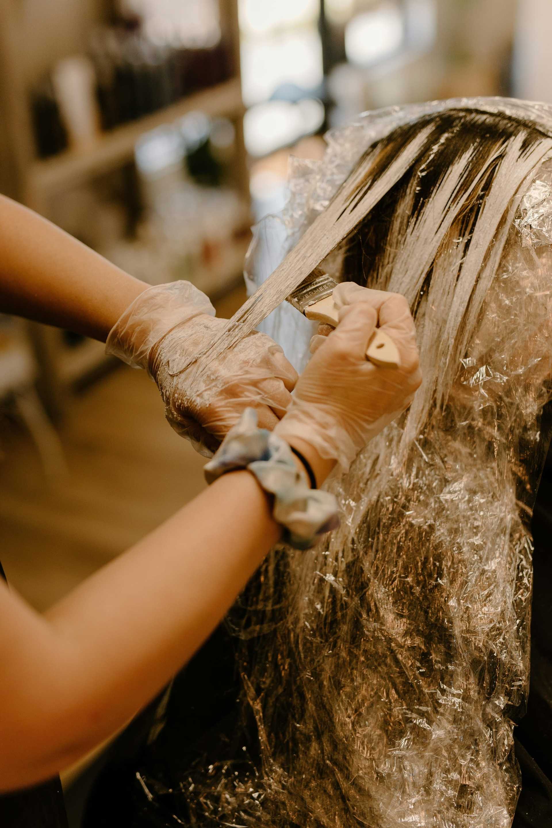Hair stylist applying dye to client's hair with brush and gloves.
