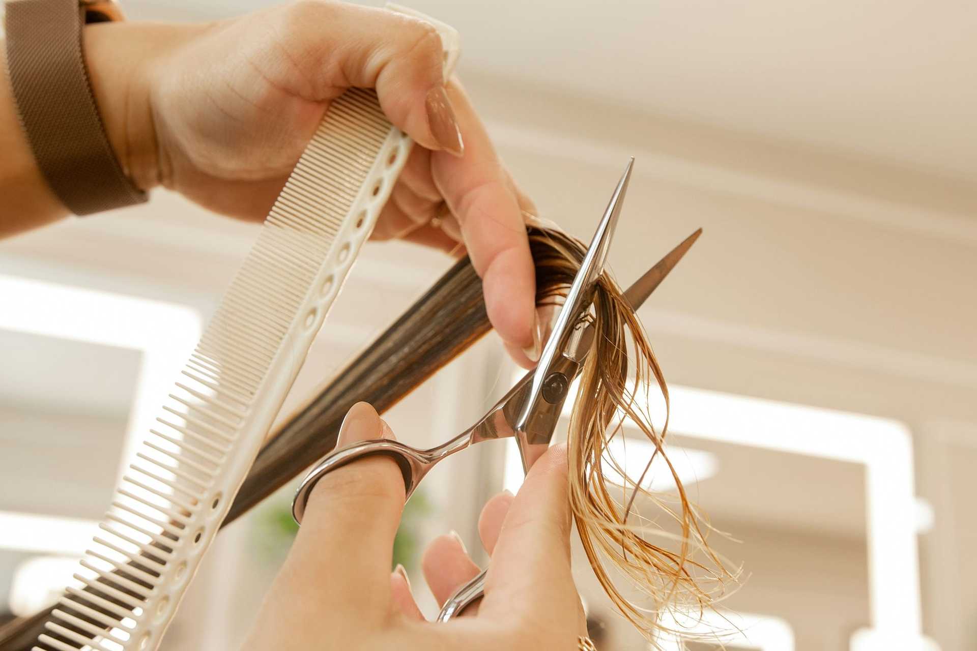 Haircutting close-up with scissors and comb trimming wet hair.