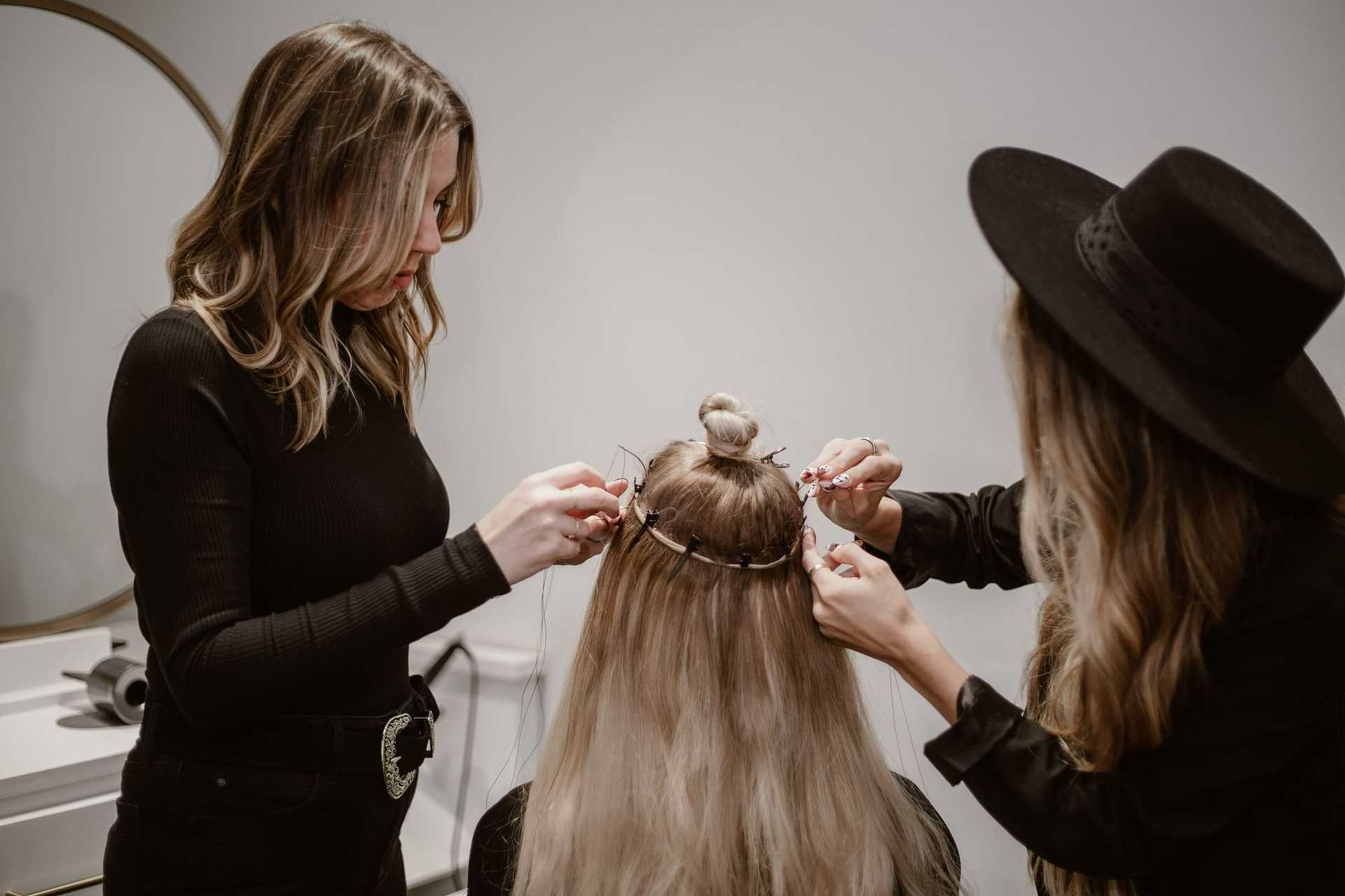 Hair stylists attaching hair extensions to a woman's head in a salon.